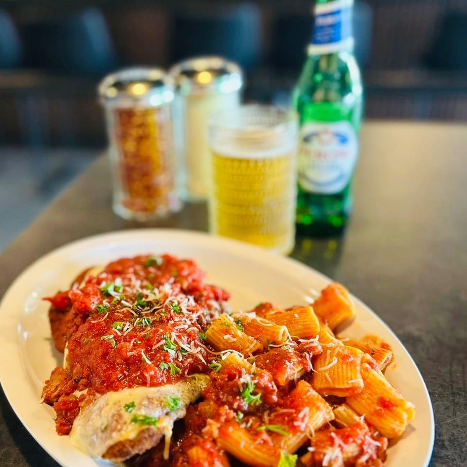 Chicken parmesan and rigatoni pasta with red sauce, cheese, and parsley, with beer.