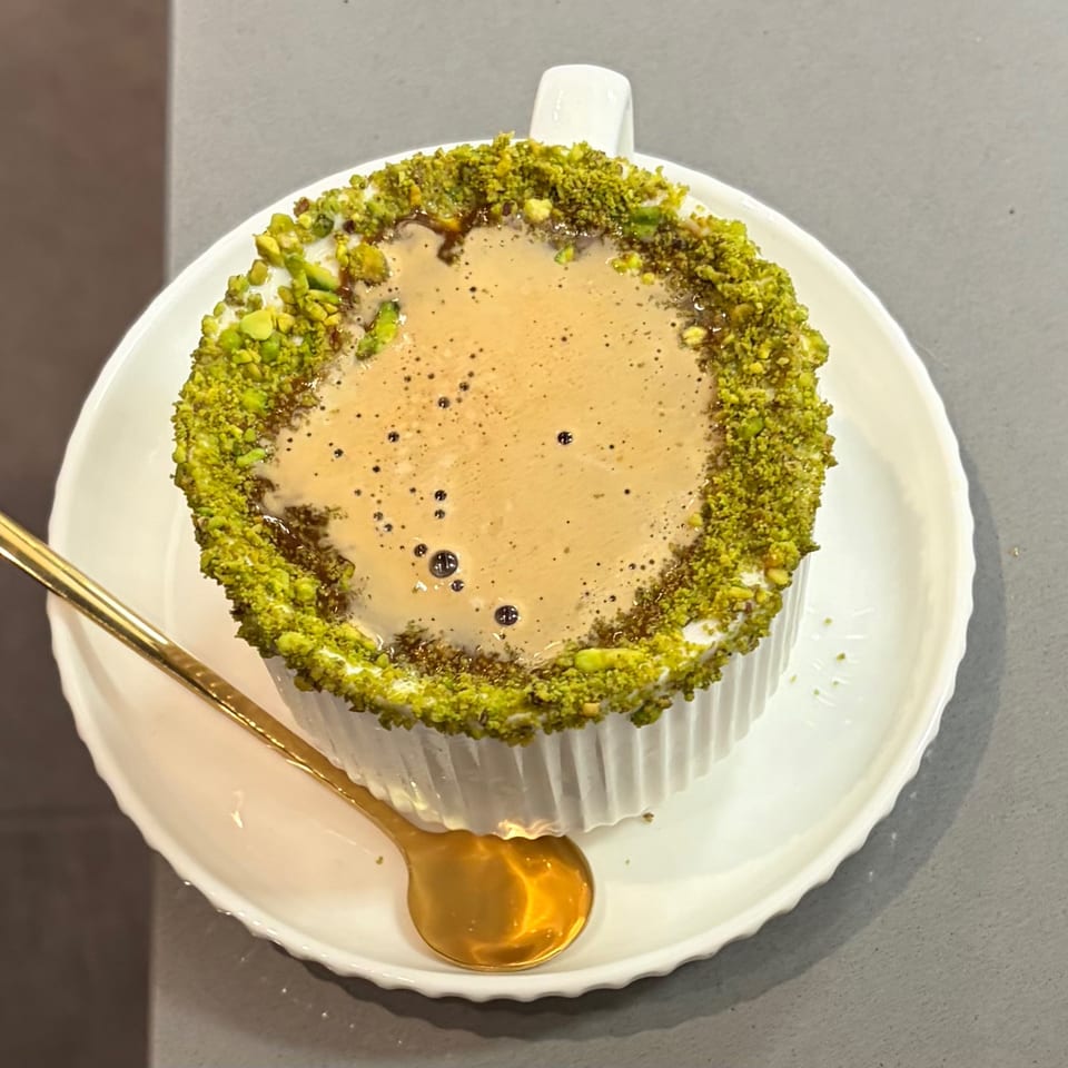 Overhead view of a coffee drink with a pistachio-crusted rim, served with a gold spoon.