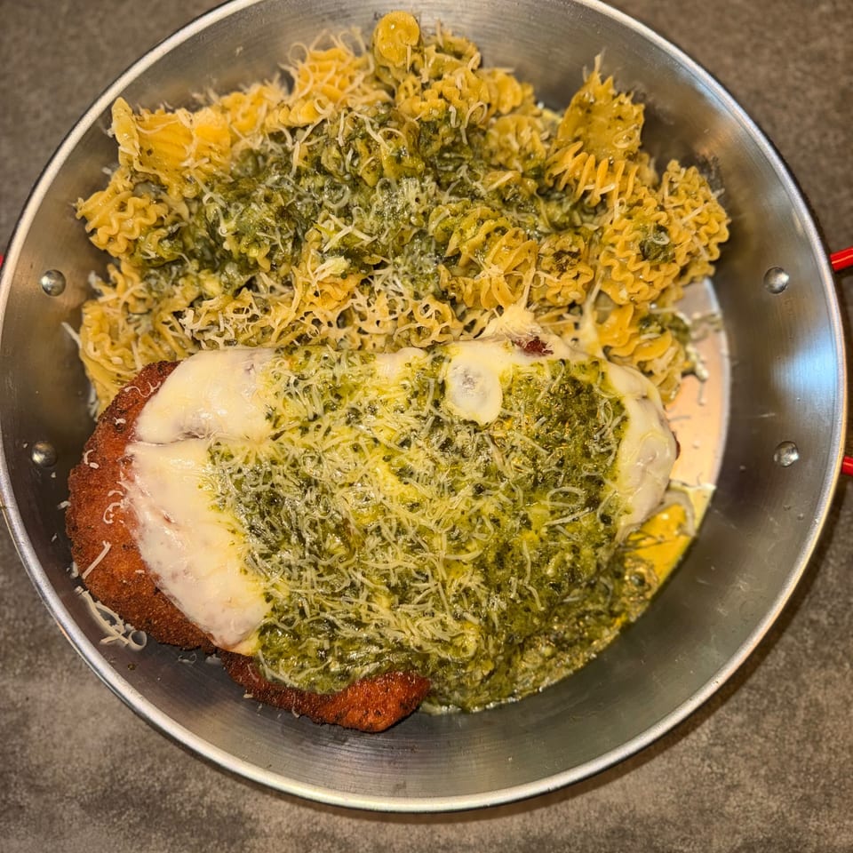 Chicken parmesan with pesto and pasta in a metal pan, topped with melted cheese.
